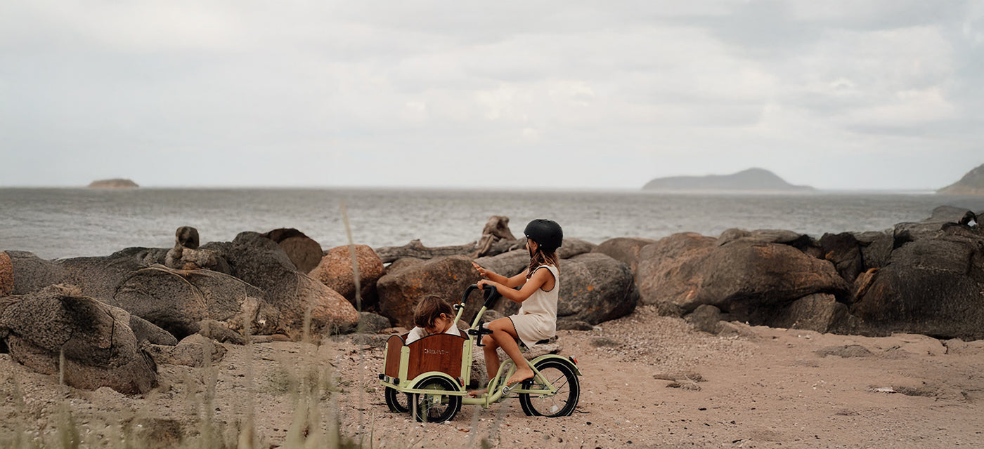 Zwei Kinder auf einem Lastenrad am Strand.