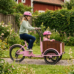 Mädchen fahren rosa Lastenrad im Garten.